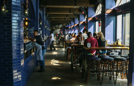 A restaurant full of people sitting at high tables on high chairs, and a staff member standing at the bar.