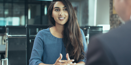Young Indian female client or candidate sitting at table, talking to senior male manager and smiling in office. 