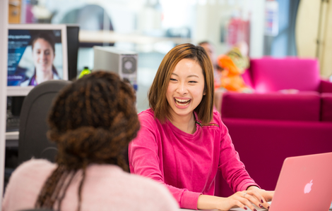 Photo of student laughing to other students while using laptop
