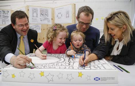 Winning Baby Box design with Graphic Design student Leanne Young with two young children and two men colouring in