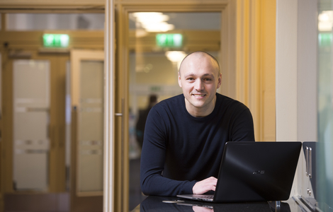 Graduate student smiling for the camera as he works on a laptop