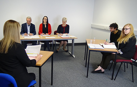Parole board oral hearing with people sitting at desks around the room