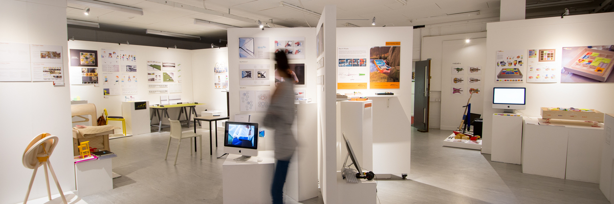 Blurred figure seen in front of students' designs at the Creative Degree Show