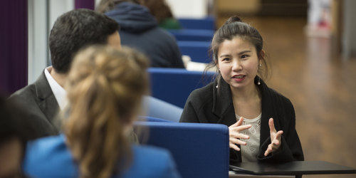 Three students talking, only one's face is visible to the camera as she uses her hands for gesturing