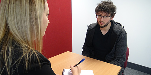 One to one interview with man sitting chatting to woman taking notes