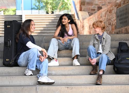 Three students sitting on the steps at Merchiston Campus, chatting