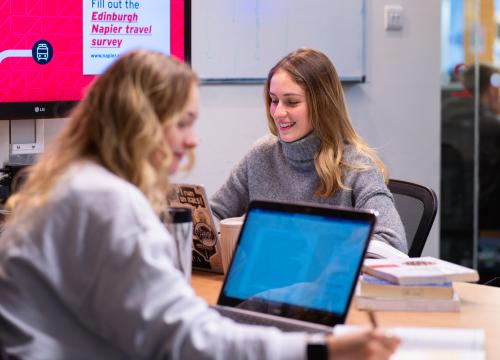 Students working on laptops around a table in a university study space.