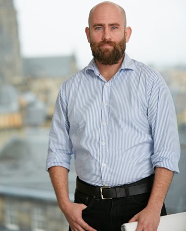 Jamie Graves standing, looking into the camera with a blurry street in the background