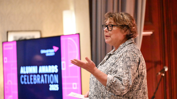 University principal, Sue Rigby, standing next to a screen stating 'Alumni Awards Celebration'
