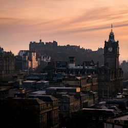 Edinburgh skyline at sunset, with the castle and clock tower silhouetted against an orange sky