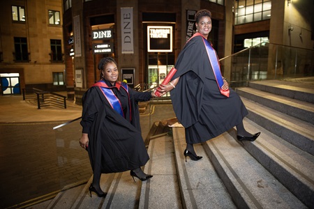 Kerry-Ann and Edwina passing a degree scroll in the style of a relay baton 