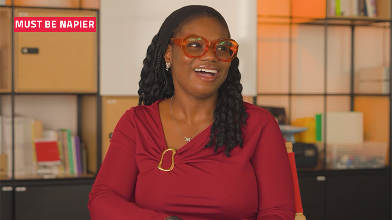 Smiling student in red top and red framed glasses with the words: Must be Napier