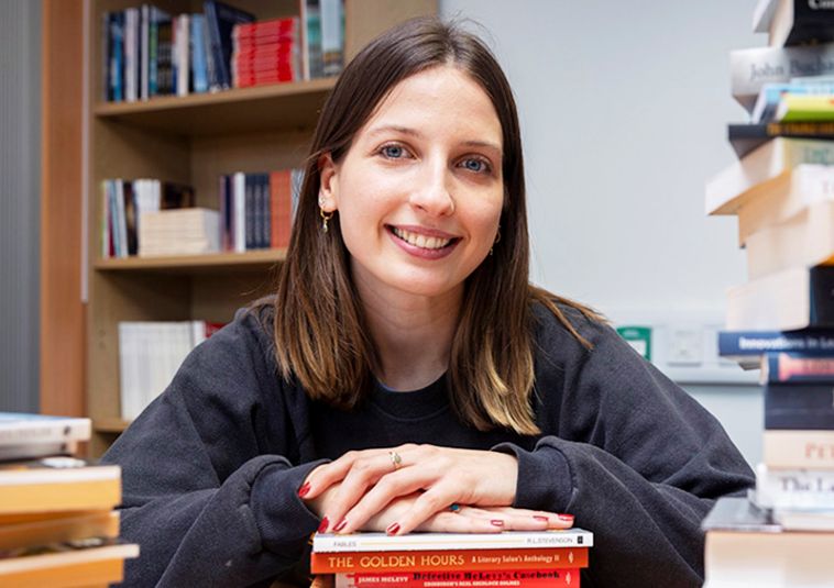 A person smiling in a room filled with books.