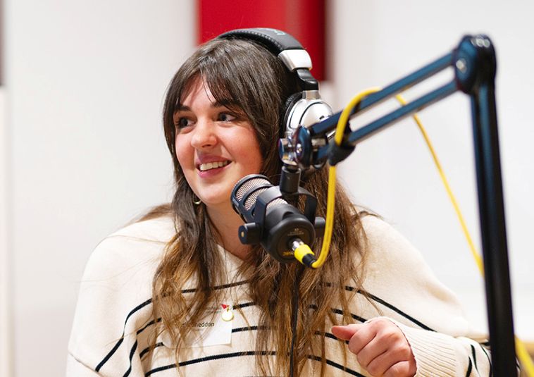 A person sitting with headphones in front of a microphone.