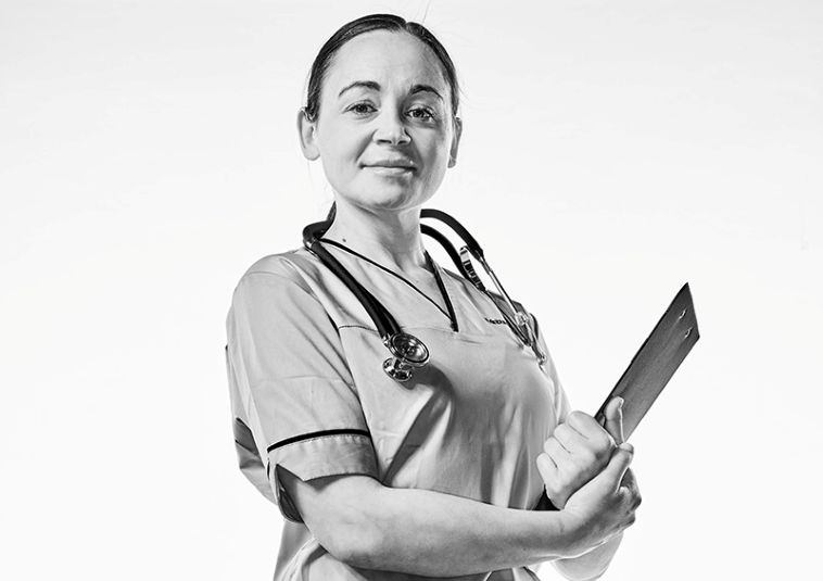 A person wearing nursing scrubs and holding a stethoscope and clipboard.