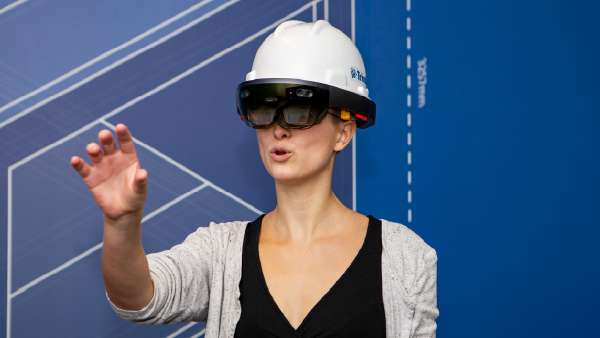 Person wearing a hard hat and augmented reality headset interacting with a virtual construction design.