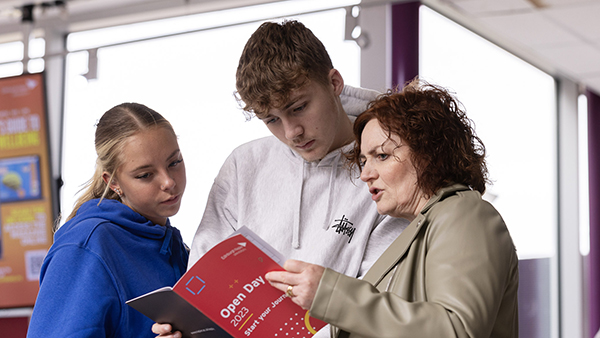 two prospective students and their parent look at the Open Day brochure