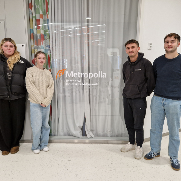 Four students standing beside a Metropolia sign indoors.