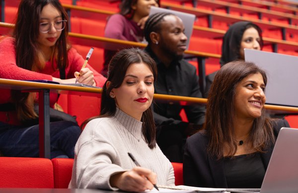 A photo of a student studying with classmates in one of our lecture halls at Sighthill campus with striking red coloured seats. 